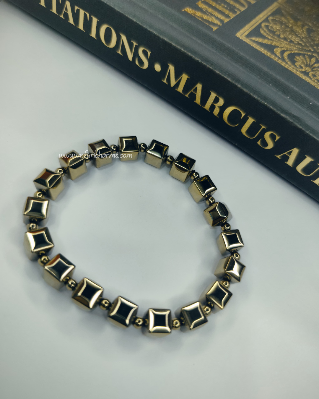 Bracelet with geometric design on a white surface with a book in the background. Luxury crystal jewelry for aura balance